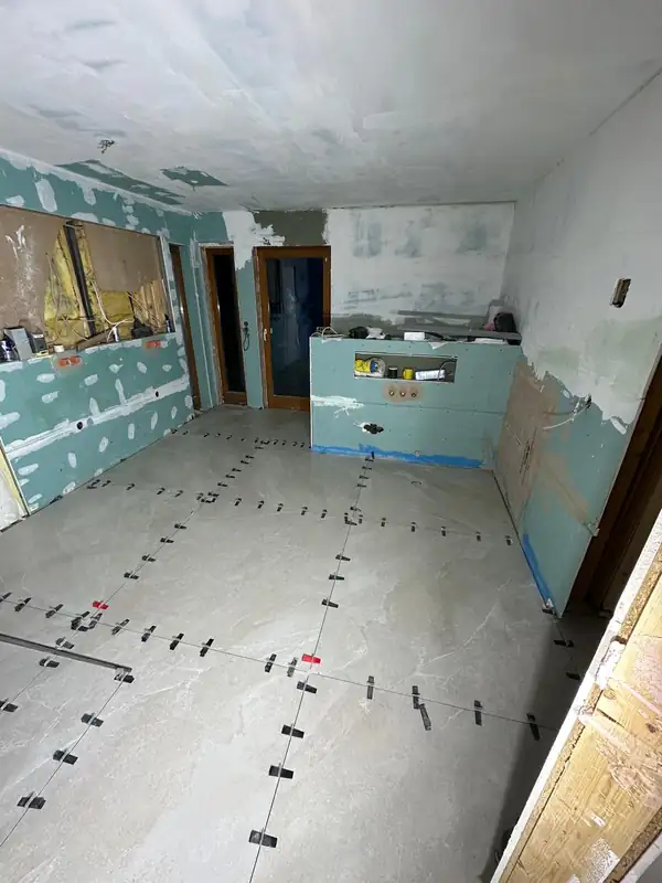 Vorher: entkerntes Badezimmer im Rohbau mit Trockenbauwänden und frisch verlegten Bodenfliesen samt Nivelliersystem