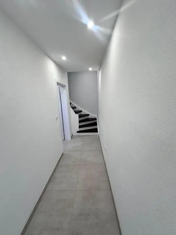 Renovierter, heller Flur einer Einliegerwohnung mit grauen Bodenfliesen, Einbaustrahlern und Treppe