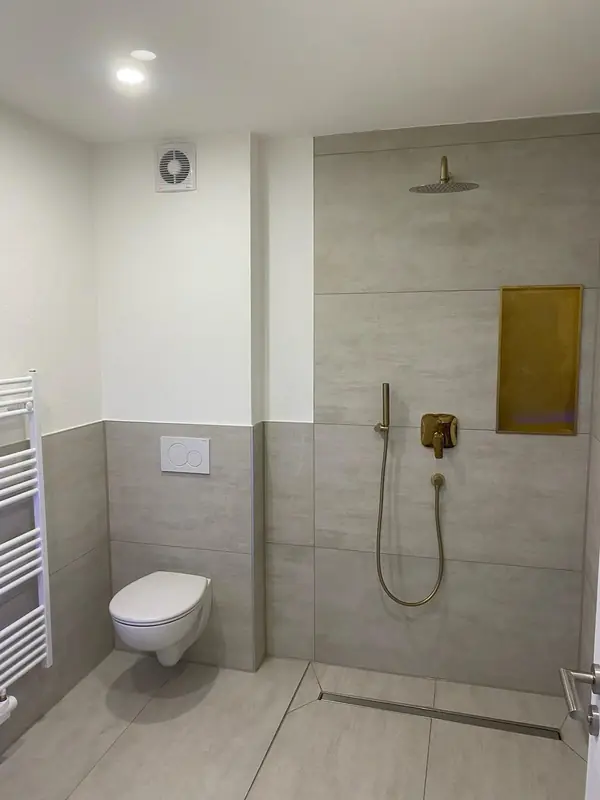 Nachher: modernes Gästebad mit Wand-WC, bodengleicher Dusche mit Ablaufrinne, goldenen Armaturen und Handtuchheizkörper